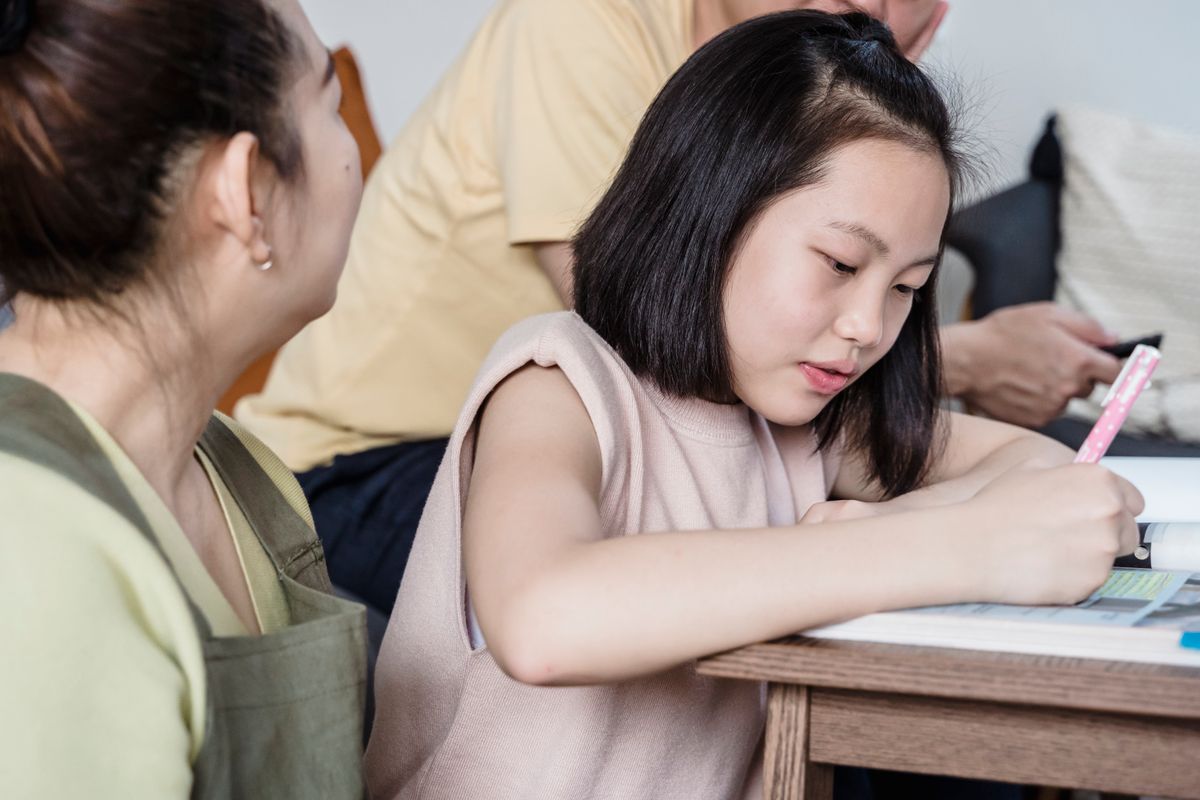 A Girl Writing on the Book while Sitting Beside Her Parents